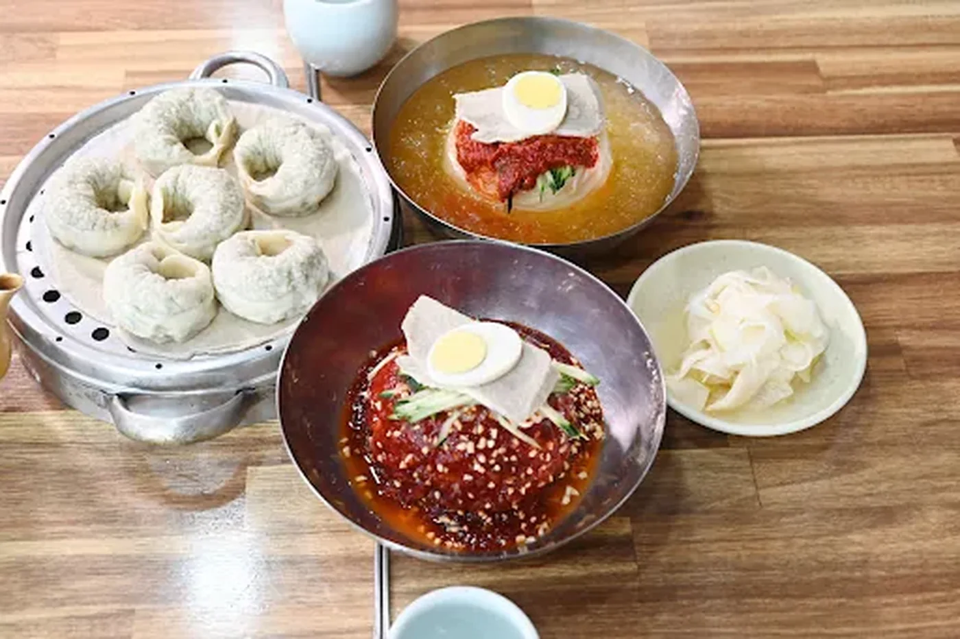 卵と赤い薬味をのせた釜山のmilmyeonが2杯、その隣に蒸し餃子
